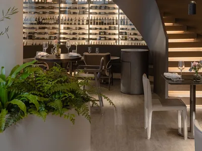 A modern restaurant bar featuring wooden materials and a spiral staircase with illuminated railings.