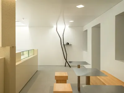 Modern restaurant interior with minimalist design featuring metal tables, wooden benches, and concrete flooring.