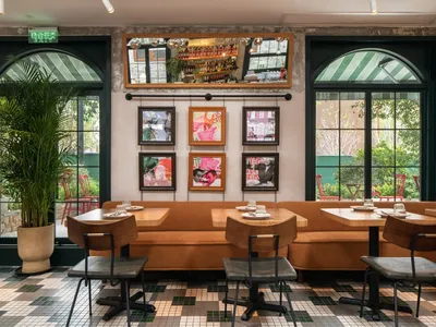 Industrial-style restaurant with a brown couch, potted plant, and framed art hanging on the wall.