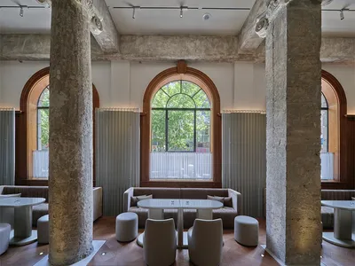 Industrial-style restaurant interior with concrete columns and an arched window.
