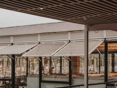 Modern industrial-style restaurant with wooden tables and chairs, glass walls overlooking a marina.