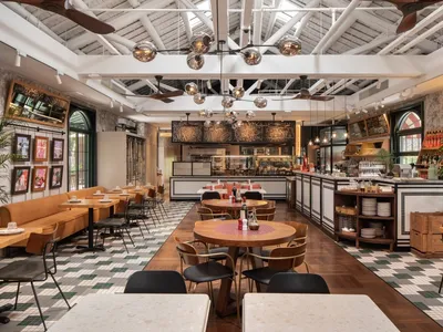 A spacious, industrial-style restaurant with wooden tables, metal chairs, concrete flooring, and ceramic tiles.
