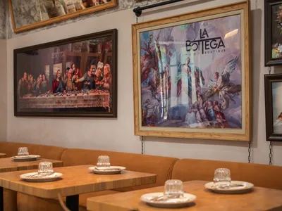 A restaurant interior with two paintings on the wall depicting a Last Supper scene and religious figures.