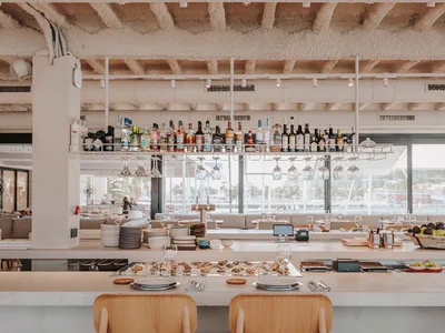 A minimalist restaurant bar with concrete walls and wooden chairs.