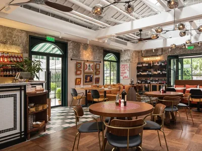 A modern cafe bar interior with wooden tables, metal chairs, and fabric seating.