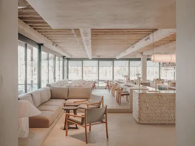 Modern restaurant interior with concrete flooring, large windows, and minimalist furniture.