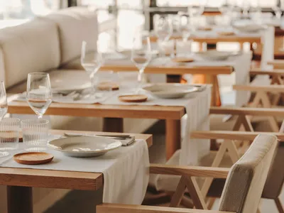 A modern restaurant interior featuring minimalist design with wooden tables and chairs.
