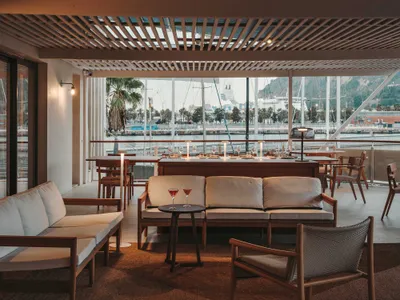 Modern restaurant bar with wooden furniture, glass tables, and fabric seating.