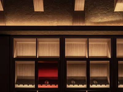 A modern restaurant bar with wooden walls, glass shelves, and a red table with bottles of wine.