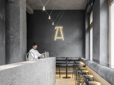 A modern restaurant interior featuring a concrete bar counter with metal stools and a minimalist design aesthetic.