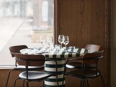 A modern dining setting with a striped table, metal-framed leather chairs, wooden walls, and large windows.