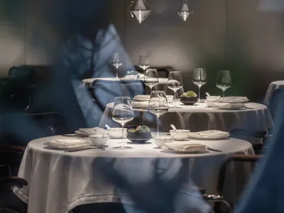 Modern restaurant interior with white tablecloths, dark wood chairs, transparent hanging lights, and green plants