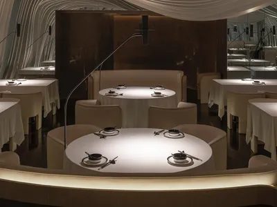 A modern restaurant interior with white textured fabric ceiling and round tables.
