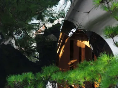 A modern restaurant interior with a circular mirrored metal sculpture and bonsai tree, offering a sophisticated dining experi