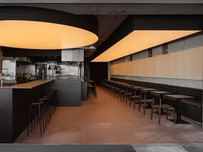 Modern minimalist restaurant interior with sleek black surfaces and concrete countertops.