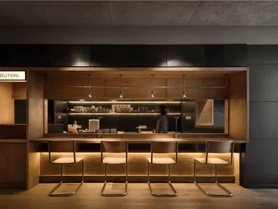 A modern, industrial-style restaurant counter with wooden seating and stainless steel accents.