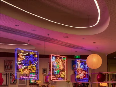 A restaurant interior with industrial design, featuring metal neon signs and vintage lighting fixtures.