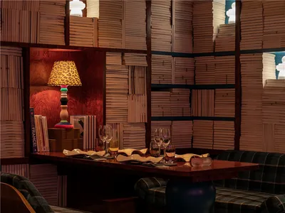 A cozy restaurant with a wooden table, bookshelf filled with books, and geometric lamp with a leopard print shade.