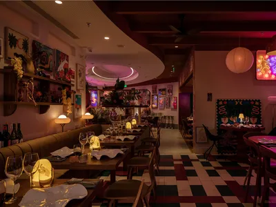 A beautifully designed restaurant interior with wooden furniture, checkered floor tiles, and colorful artwork on the walls.