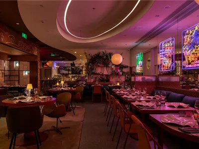 A modern restaurant interior with red lighting, fabric seating, and plants.