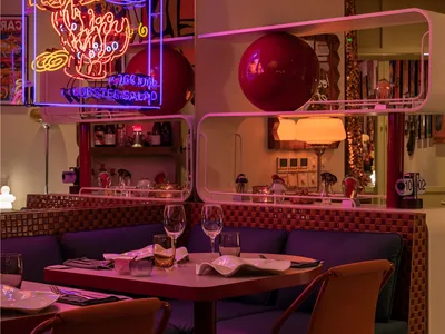 Modern restaurant interior with red and purple lighting, fabric seating, and wood accents