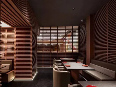 A modern restaurant interior with wooden paneled walls, white upholstered seating, and red plates on the tables.