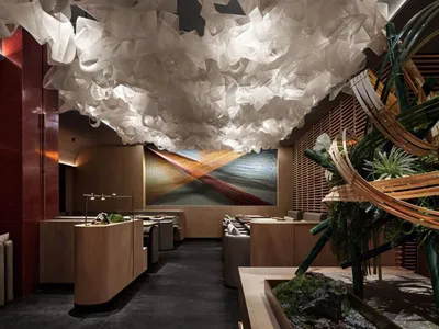 Modern restaurant interior with a white organic cloud ceiling, bamboo structure, and a waterfall fountain centered on a red a