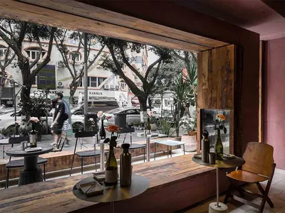 Interior view of a cafe bar with wooden tables, chairs, and decorations, with street view seen through a window.