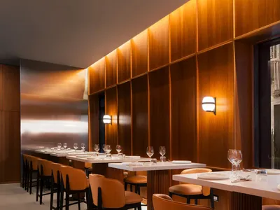 A modern restaurant interior featuring wooden walls and furniture with white countertops and orange stools.
