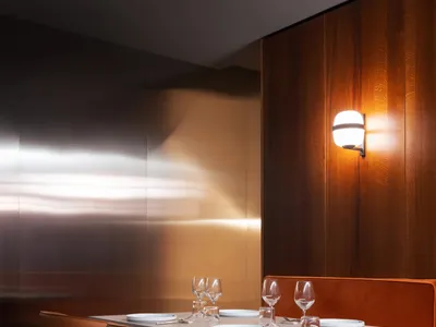 A modern restaurant interior featuring a table set for two with wooden seating and a spotlight on the wall.
