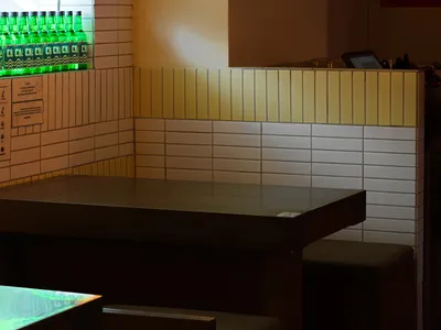 A dimly lit restaurant interior with a metal and concrete bar counter, tile backsplash, and vintage lightbulb hanging fixture