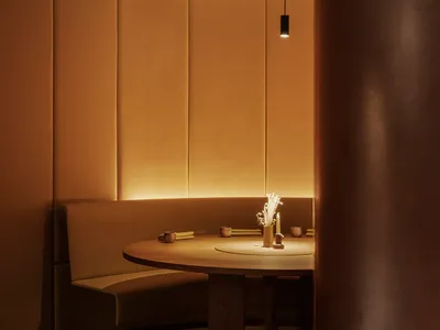 A minimalist restaurant dining room with a round wooden table, leather seating, and warm lighting.