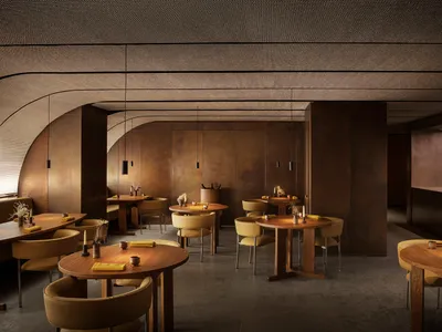 Modern restaurant interior with round wooden tables, yellow cushions, and minimalistic decor.