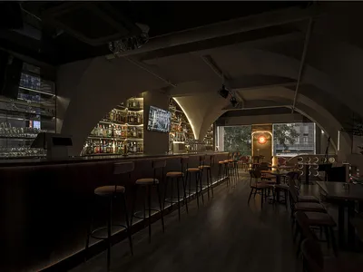 A modern bar interior with wooden and concrete materials and high stools at the bar.
