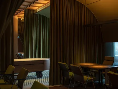Industrially styled restaurant interior with green curtains, wooden tables, and metal chairs