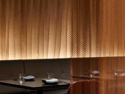 A modern restaurant interior featuring textured fabric curtains and a booth-style seating arrangement.