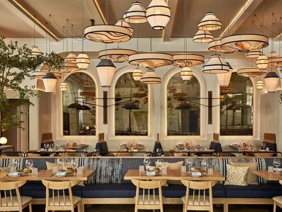 A modern restaurant interior with wooden tables, upholstered benches, and hanging pendant lights.