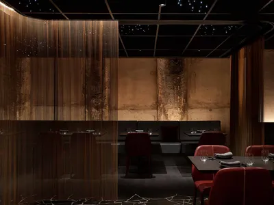 A modern restaurant interior with metal acoustic curtains, dark marble flooring, and dark furniture.
