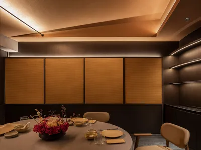 Modern restaurant interior design featuring wooden paneling, round table with plates, glasses, and floral centerpiece.