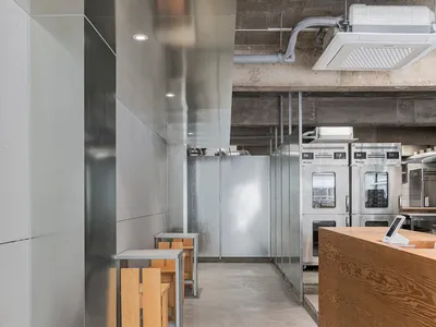 Industrial-style restaurant interior with metal walls, concrete flooring, and wooden tables and stools.