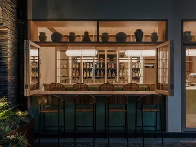 A modern restaurant bar with wooden stools, glass shelves, and metal accents.