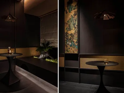 A modern restaurant interior with dark wood, suede, and woven-fiber materials, featuring a dark table with a glass and a smal