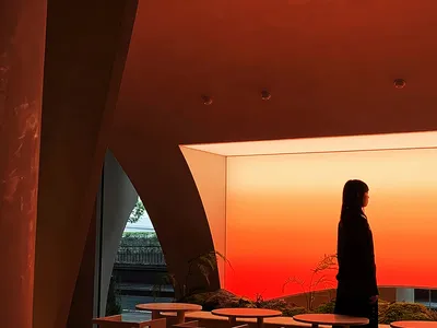 Person standing in a modern restaurant interior with red lighting and contemporary furniture.