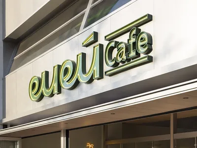 Outdoor seating area of a modern cafe with white marble ground and green signage.