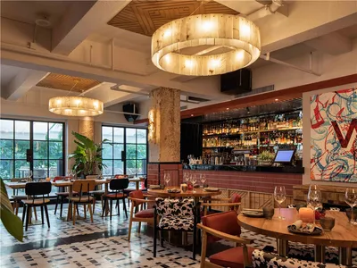 Modern restaurant interior with wooden tables and chairs, large pendant lights, and a well-stocked bar.