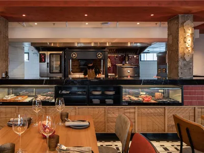 A modern restaurant interior featuring wooden tables, concrete pillars, and glass displays.