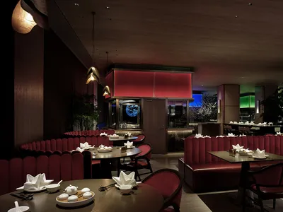 A modern restaurant interior with red leather booths, round tables, and white tablecloths.