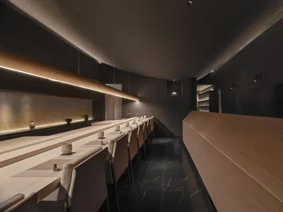 A minimalist restaurant interior with a wooden countertop and marble floor.