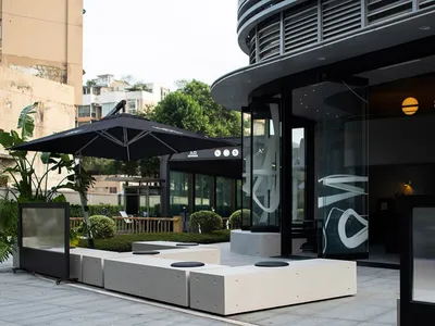 Modern restaurant exterior with metal accents, large glass windows, concrete seating, and green plants