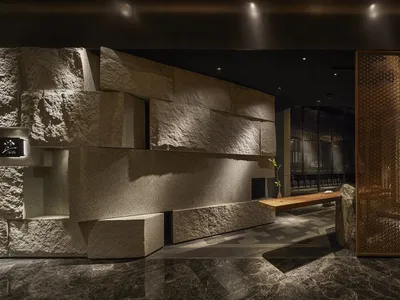 Modern restaurant interior with metal perforated panel, stone accent wall, and marble flooring.